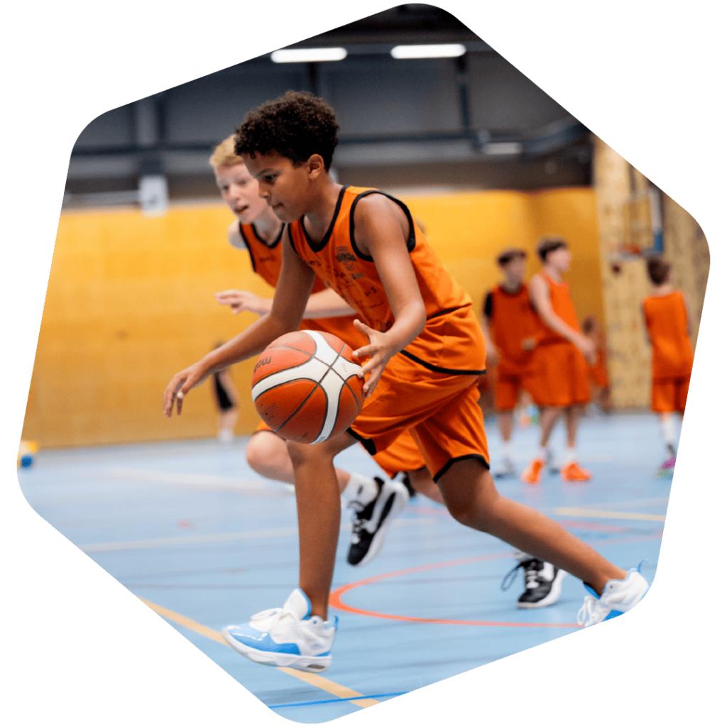 Kinderen spelen basketbal tijdens een sportief basketbalfeestje van VoetbalSkills in de sporthal.