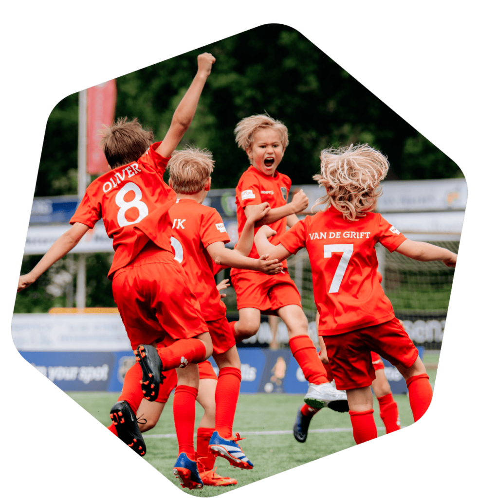 Vier juichende voetballers in rode tenues op het voetbalveld tijdens de Skills Voetbaldagen.