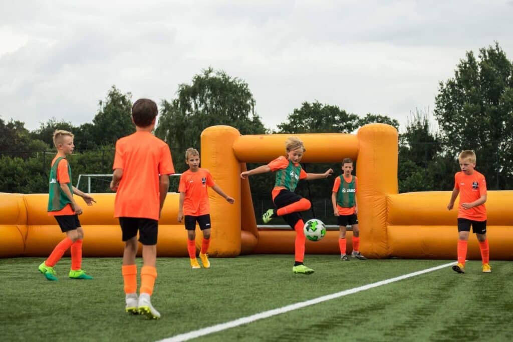 Kinderen spelen een wedstrijd in een opblaasbaar voetbalveld tijdens een voetbalclinic kinderfeestje van VoetbalSkills.