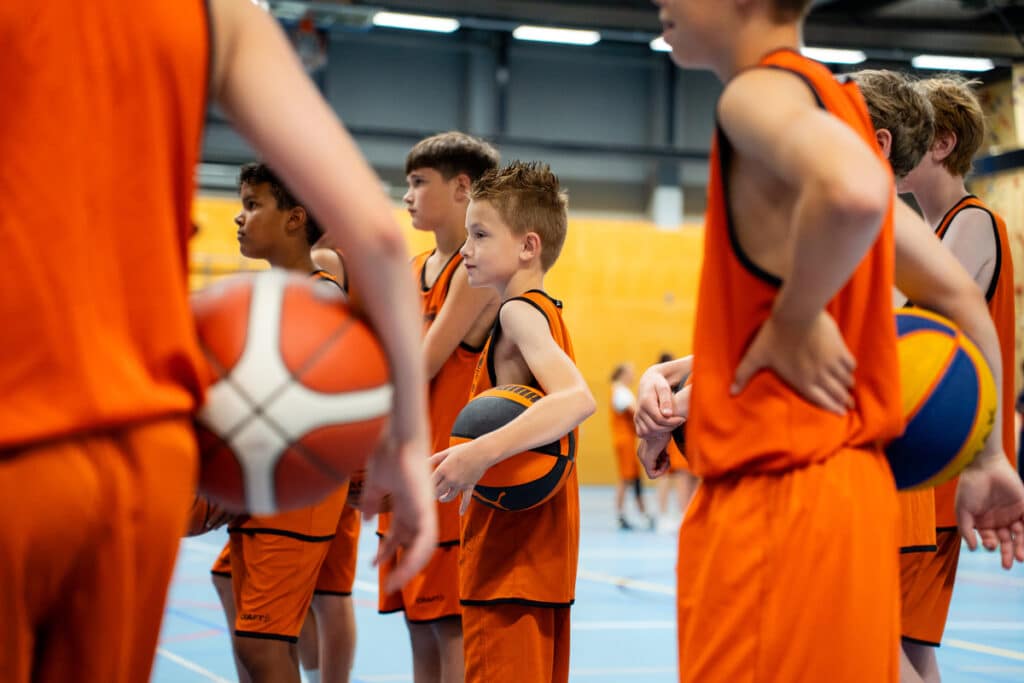 Groep jonge basketballers met basketbal in de hand tijdens een trainingsmoment voor promotie basketbalvacature