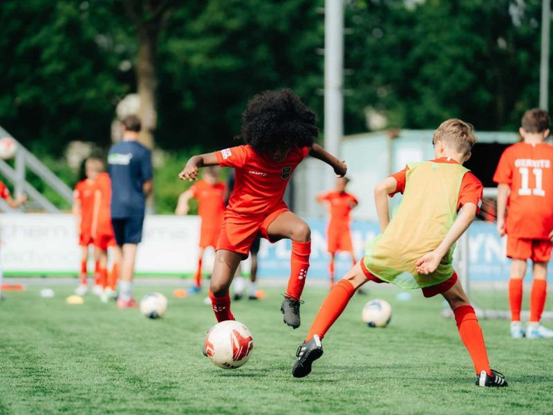 Jonge voetballers trainen techniek en balcontrole tijdens Skills Voetbaldagen op het voetbalveld.
