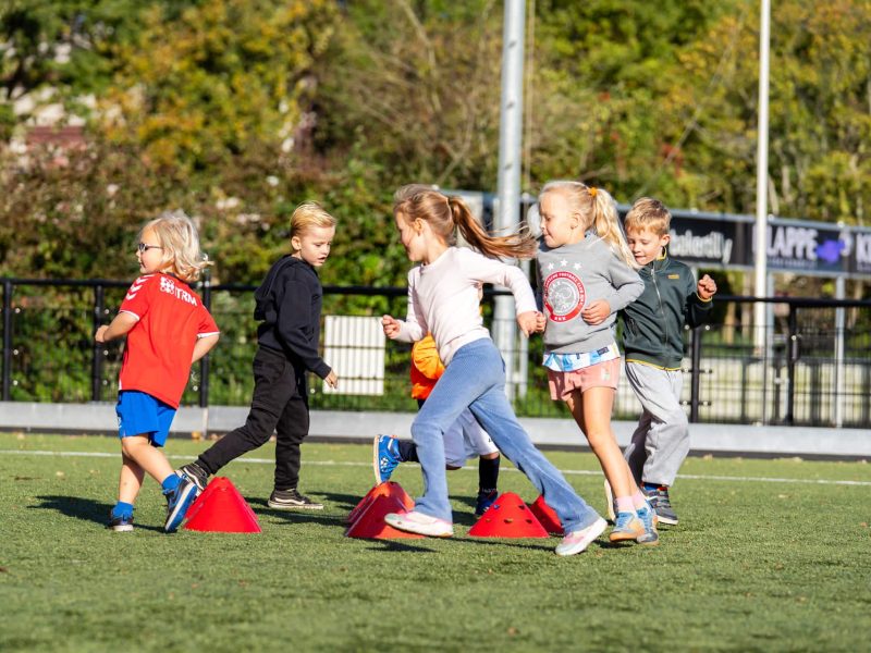 Jonge kinderen bewegen spelenderwijs tijdens een Sportieve Studiedag van FC VoetbalSkills op het sportveld.